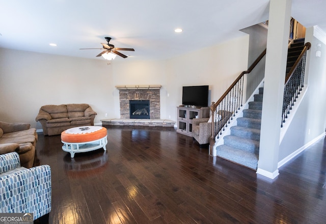 living room with dark hardwood / wood-style flooring, ceiling fan, and a stone fireplace