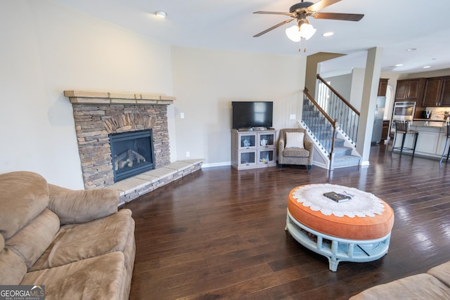 living room with ceiling fan, dark hardwood / wood-style flooring, and a stone fireplace