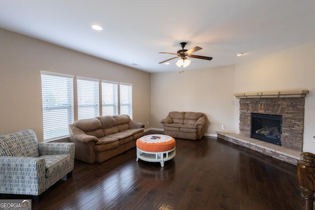 living room with ceiling fan, dark hardwood / wood-style flooring, and a stone fireplace