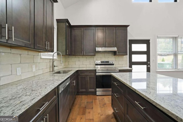 kitchen featuring appliances with stainless steel finishes, light stone countertops, dark brown cabinets, dark hardwood / wood-style floors, and sink