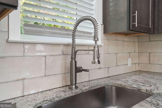 room details with light stone countertops, dark brown cabinets, backsplash, and sink