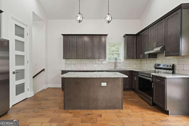 kitchen with pendant lighting, lofted ceiling, appliances with stainless steel finishes, light stone countertops, and light hardwood / wood-style floors