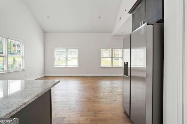 kitchen featuring light wood-type flooring, dark brown cabinets, high vaulted ceiling, stainless steel refrigerator with ice dispenser, and light stone countertops