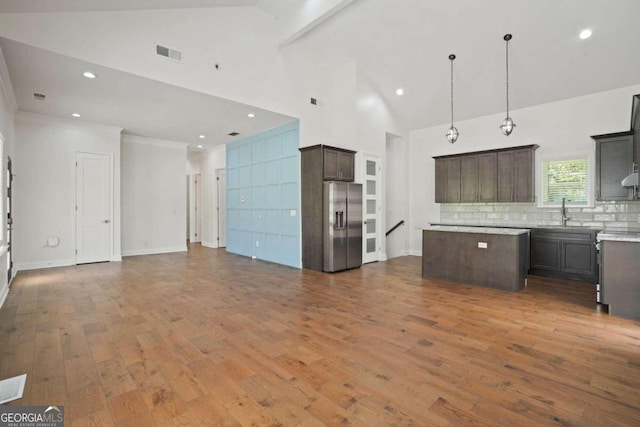 kitchen with appliances with stainless steel finishes, high vaulted ceiling, pendant lighting, a center island, and hardwood / wood-style flooring