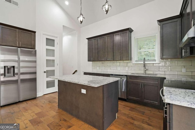 kitchen with appliances with stainless steel finishes, tasteful backsplash, a kitchen island, decorative light fixtures, and sink