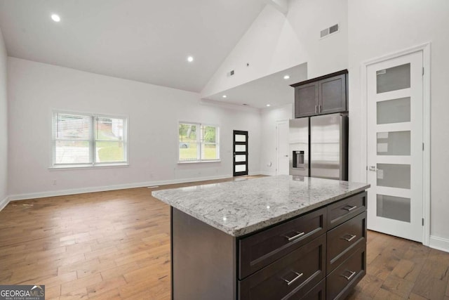 kitchen featuring light stone counters, a center island, stainless steel refrigerator with ice dispenser, high vaulted ceiling, and dark hardwood / wood-style flooring