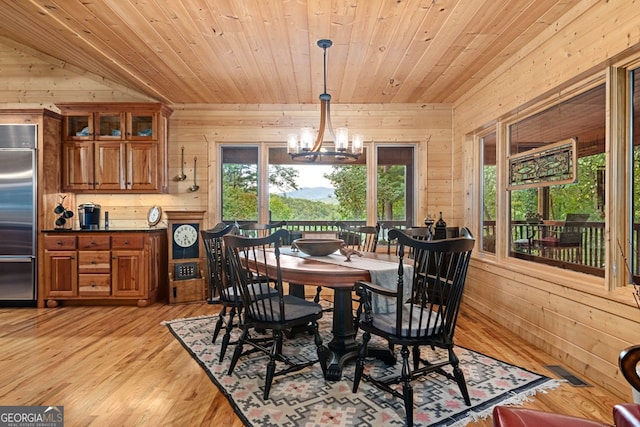 dining room featuring a notable chandelier, wood walls, light hardwood / wood-style floors, and a wealth of natural light