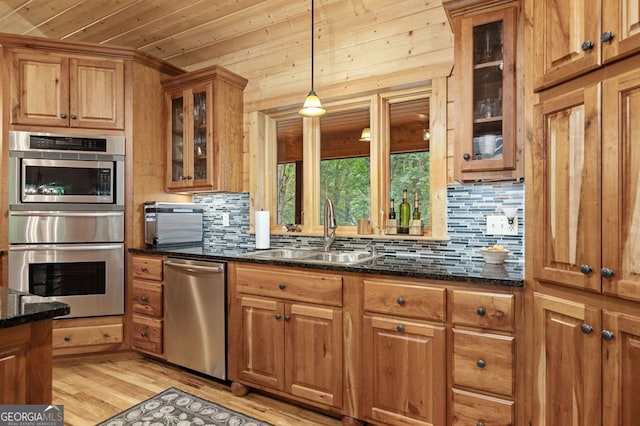 kitchen featuring sink, decorative light fixtures, appliances with stainless steel finishes, dark stone counters, and light hardwood / wood-style floors