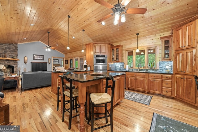 kitchen with ceiling fan, a stone fireplace, light hardwood / wood-style flooring, and wooden ceiling