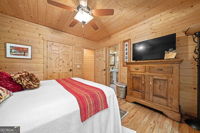 bedroom featuring light hardwood / wood-style flooring, wooden walls, ceiling fan, and connected bathroom