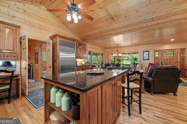 kitchen featuring stainless steel built in refrigerator, wooden walls, light hardwood / wood-style floors, and ceiling fan with notable chandelier