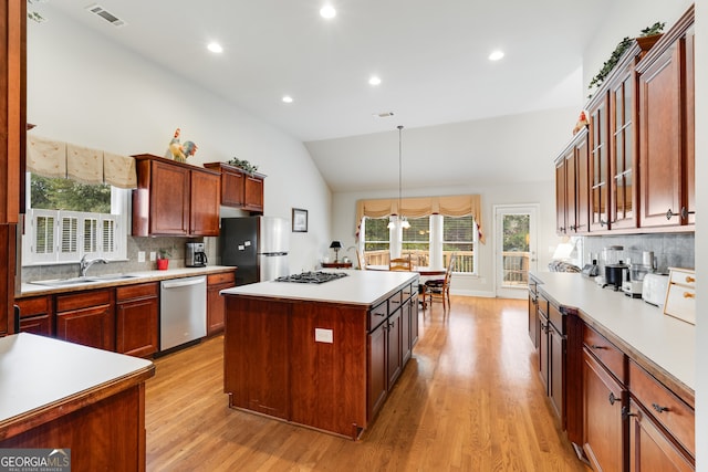 kitchen featuring a kitchen island, vaulted ceiling, appliances with stainless steel finishes, light hardwood / wood-style floors, and tasteful backsplash