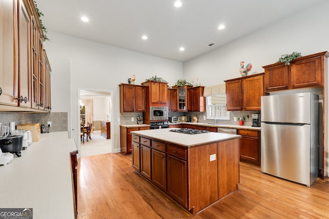 kitchen with stainless steel appliances, sink, light wood-type flooring, and a kitchen island