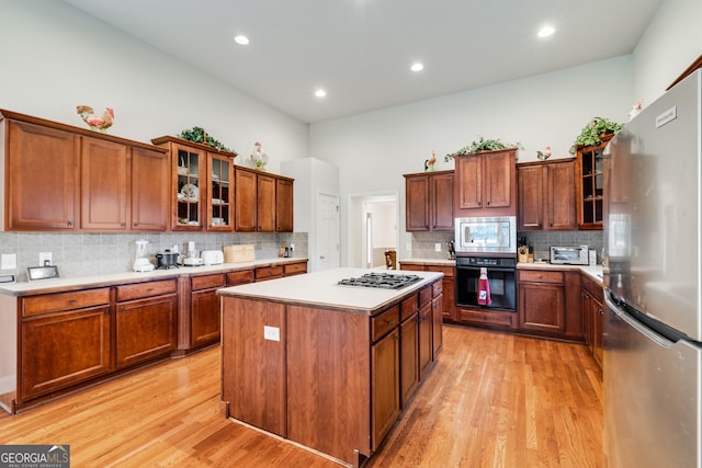 kitchen with tasteful backsplash, appliances with stainless steel finishes, light wood-type flooring, and a kitchen island