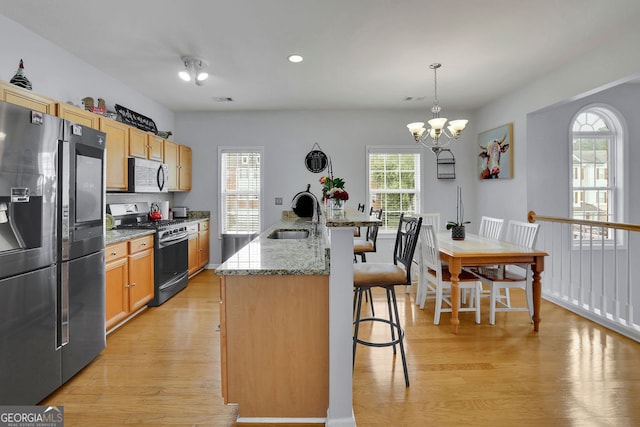 kitchen featuring sink, decorative light fixtures, a kitchen island with sink, stainless steel appliances, and light wood-type flooring