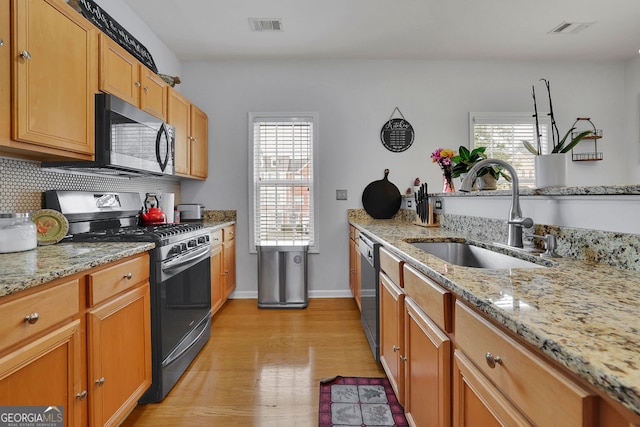 kitchen with sink, light hardwood / wood-style flooring, stainless steel appliances, decorative backsplash, and light stone countertops