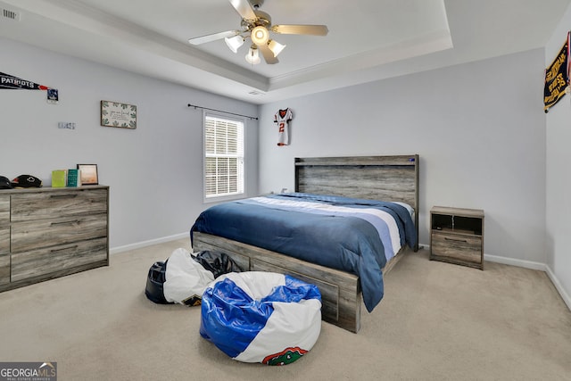 bedroom with a raised ceiling, ceiling fan, and light colored carpet