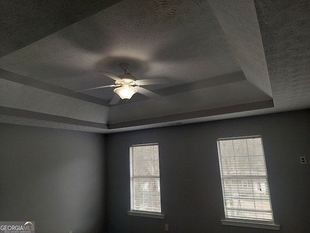 details with ceiling fan, a raised ceiling, and a textured ceiling