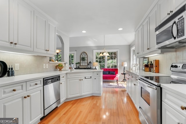 kitchen featuring appliances with stainless steel finishes, light wood-type flooring, white cabinetry, and decorative light fixtures