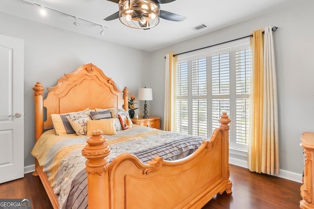 bedroom with track lighting, multiple windows, ceiling fan, and dark hardwood / wood-style flooring