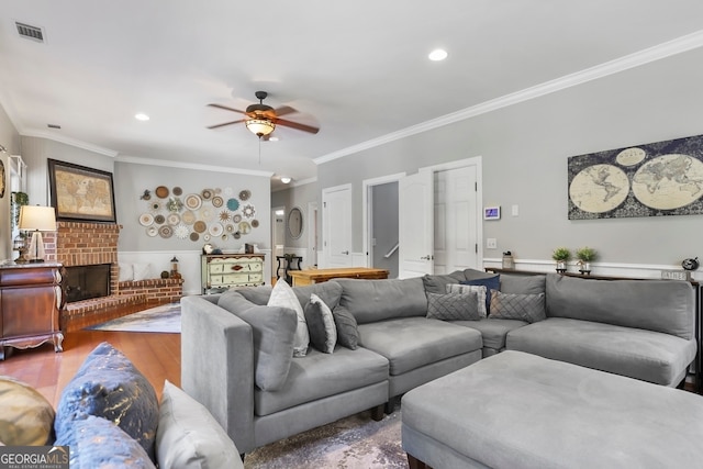 living room with ceiling fan, a brick fireplace, ornamental molding, and wood-type flooring