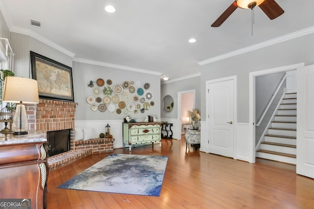 living room with hardwood / wood-style flooring, crown molding, ceiling fan, and a fireplace