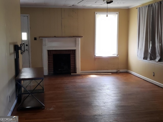 unfurnished living room with crown molding, a brick fireplace, dark hardwood / wood-style floors, and wooden walls