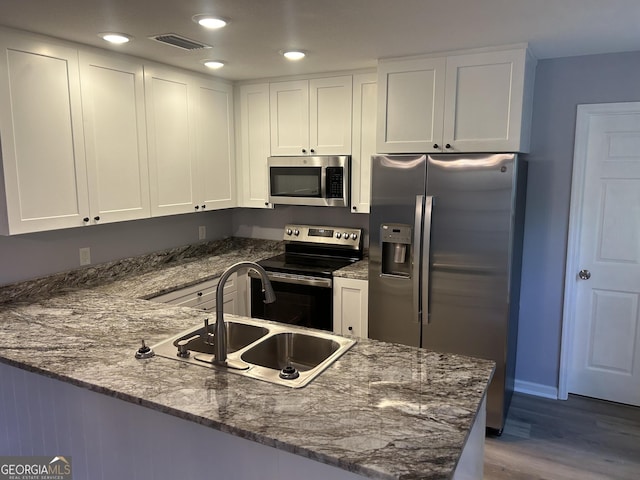 kitchen featuring dark stone countertops, stainless steel appliances, kitchen peninsula, and white cabinetry