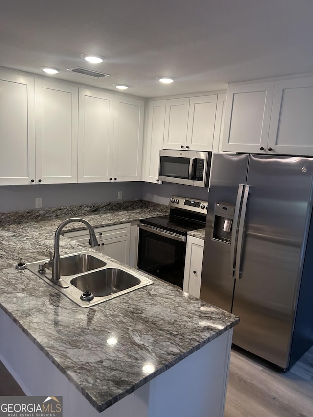 kitchen with white cabinets, sink, light hardwood / wood-style flooring, stainless steel appliances, and dark stone countertops