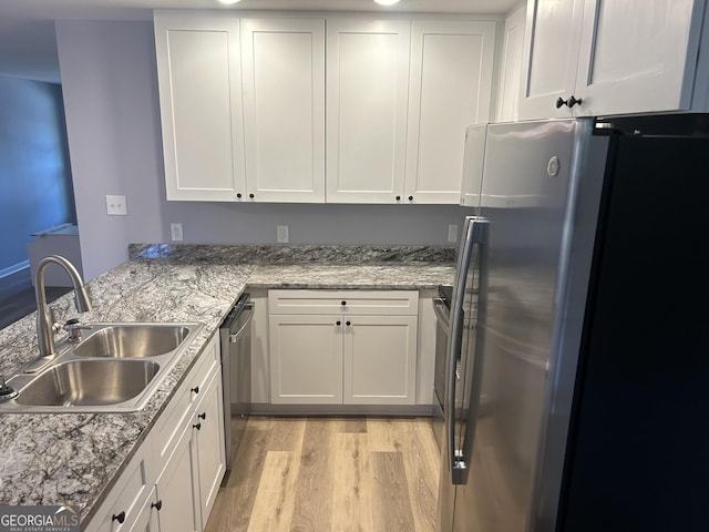 kitchen with light stone countertops, white cabinets, sink, light hardwood / wood-style floors, and appliances with stainless steel finishes