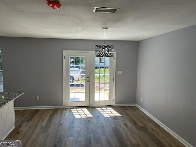 unfurnished dining area with a notable chandelier, dark wood-type flooring, french doors, and a textured ceiling