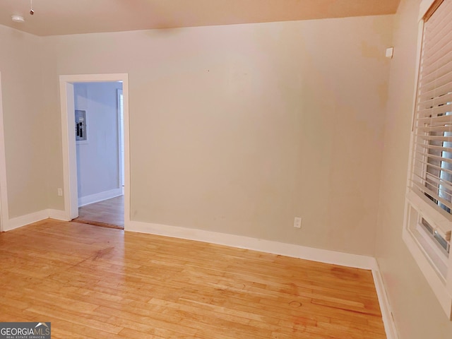 spare room with electric panel, light wood-style flooring, and baseboards