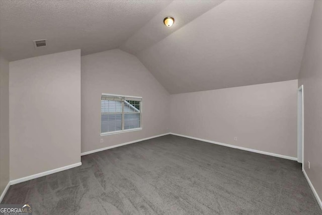 additional living space with dark carpet, lofted ceiling, and a textured ceiling