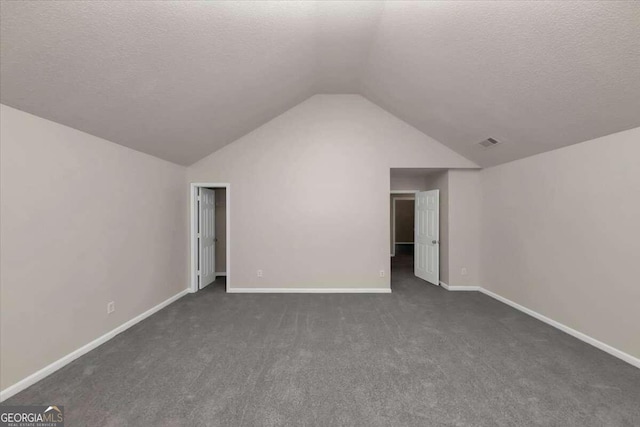 additional living space with dark colored carpet, lofted ceiling, and a textured ceiling