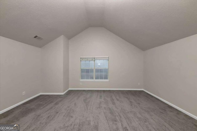 additional living space featuring dark carpet, a textured ceiling, and lofted ceiling