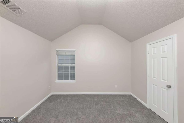 additional living space with dark carpet, a textured ceiling, and vaulted ceiling