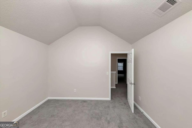 interior space featuring a textured ceiling, vaulted ceiling, and light carpet