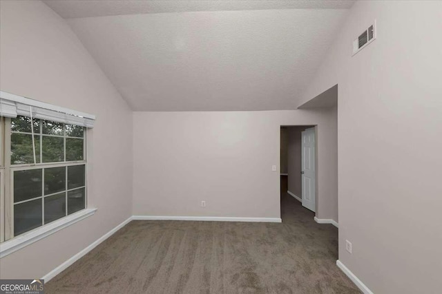 spare room with a textured ceiling, carpet, and vaulted ceiling