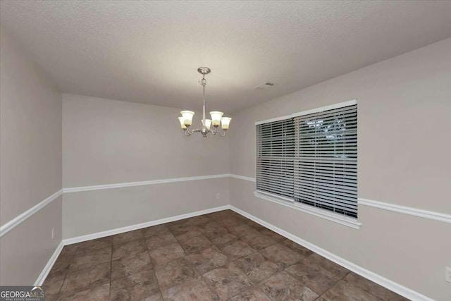 spare room featuring a notable chandelier and a textured ceiling