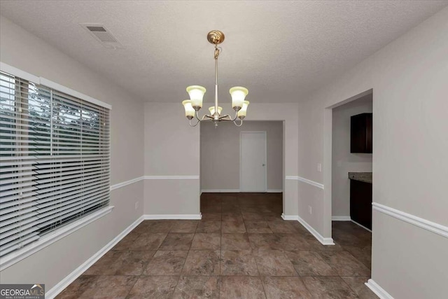 unfurnished dining area with a notable chandelier and a textured ceiling