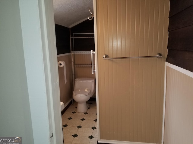 bathroom featuring a textured ceiling, toilet, lofted ceiling, and wood walls