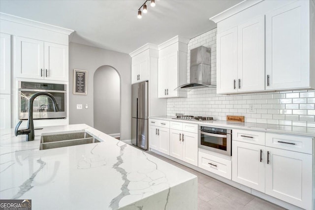 kitchen with light stone countertops, stainless steel appliances, wall chimney range hood, and white cabinetry