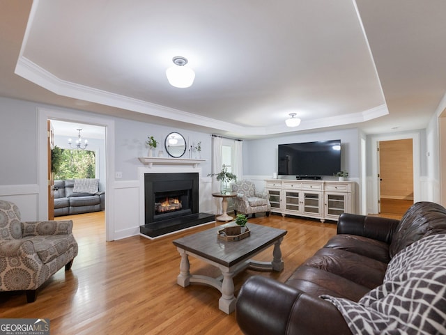 living room featuring a raised ceiling, ornamental molding, wood-type flooring, and an inviting chandelier