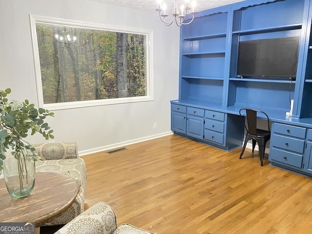 office space featuring built in features, light hardwood / wood-style flooring, a chandelier, a textured ceiling, and built in desk