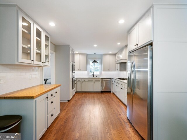 kitchen featuring pendant lighting, wood counters, premium range hood, appliances with stainless steel finishes, and white cabinetry