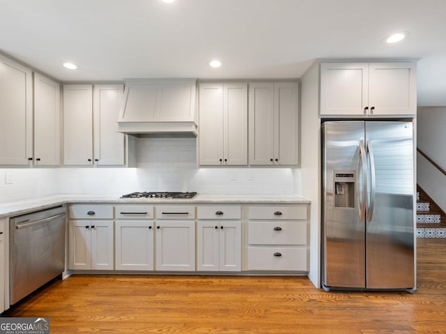 kitchen with light hardwood / wood-style flooring, white cabinets, stainless steel appliances, and custom exhaust hood