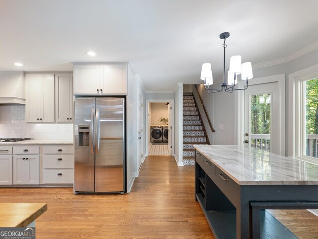 kitchen featuring appliances with stainless steel finishes, wall chimney range hood, pendant lighting, washing machine and clothes dryer, and white cabinetry