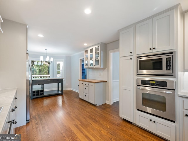 kitchen featuring decorative backsplash, stainless steel appliances, a notable chandelier, white cabinetry, and hanging light fixtures