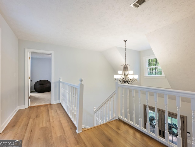 hallway with light hardwood / wood-style floors, lofted ceiling, and an inviting chandelier