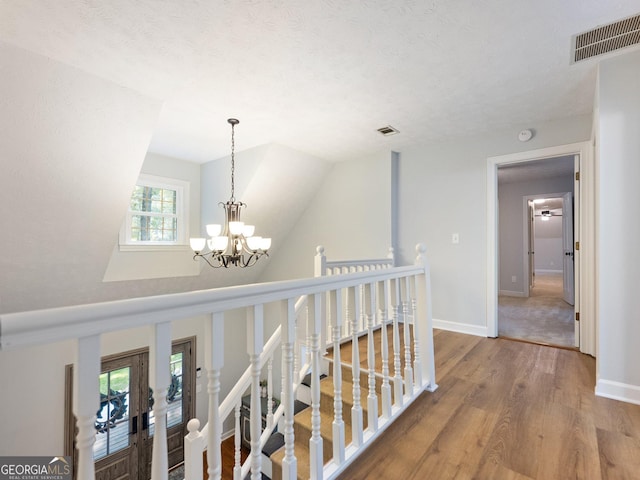 corridor with hardwood / wood-style floors, a textured ceiling, and an inviting chandelier